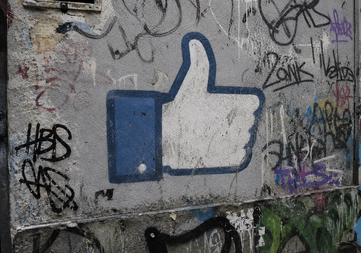 Urban wall covered in graffiti and stencilled, blue thumbs-up icon