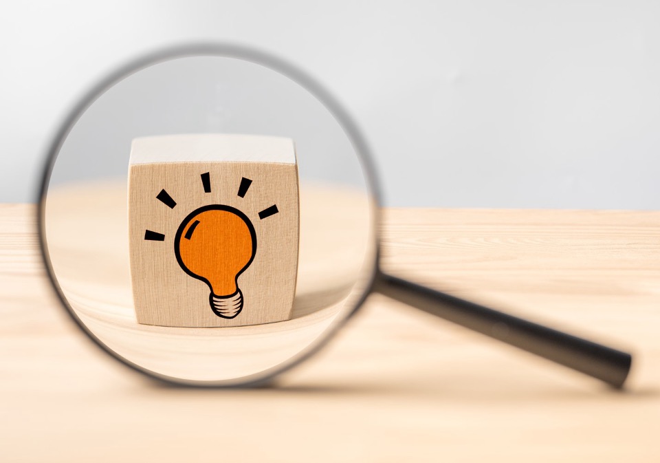 Magnifying glass looking at a wooden cube with a lightbulb symbol